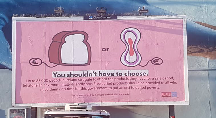 Photo of a billboard with an image of bread and a period pad with price tags attached. Below says, 'You shouldn't have to choose.'